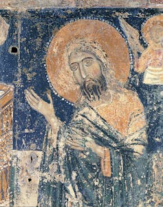 A fresco of Christ with lifted arms, his head encircled by a halo, or nimbus, wearing a tunic and a mantle.